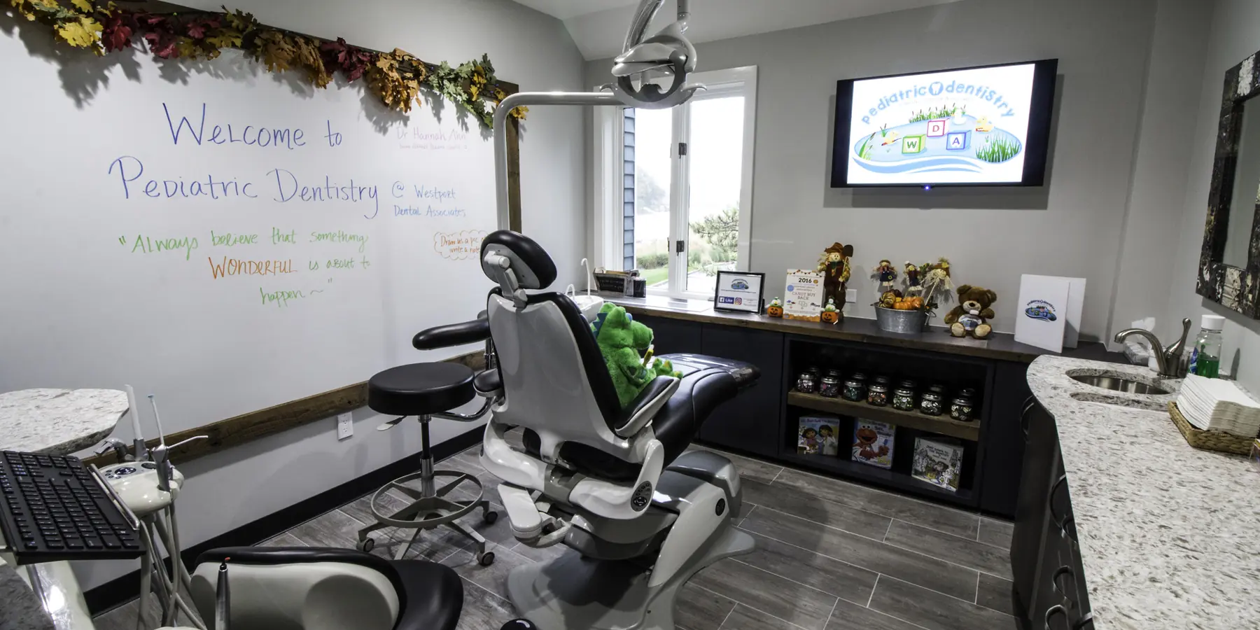 The pediatric treatment room at Westport Dental Associates, with its welcome board and toy shelf.